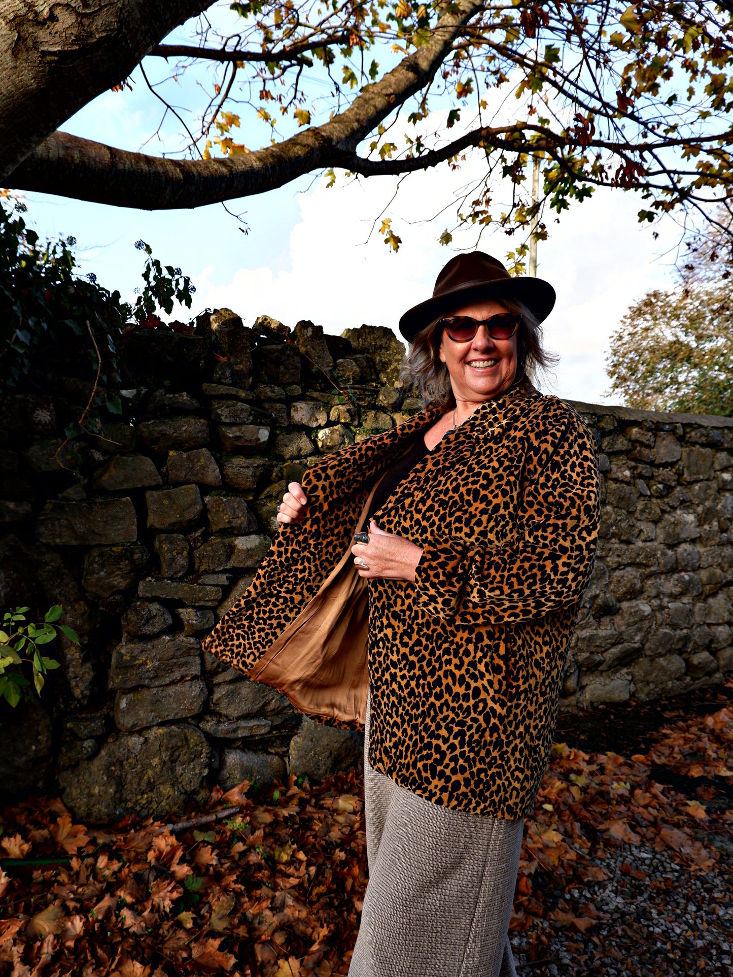 Person wearing a leopard print coat and hat standing against a stone wall
