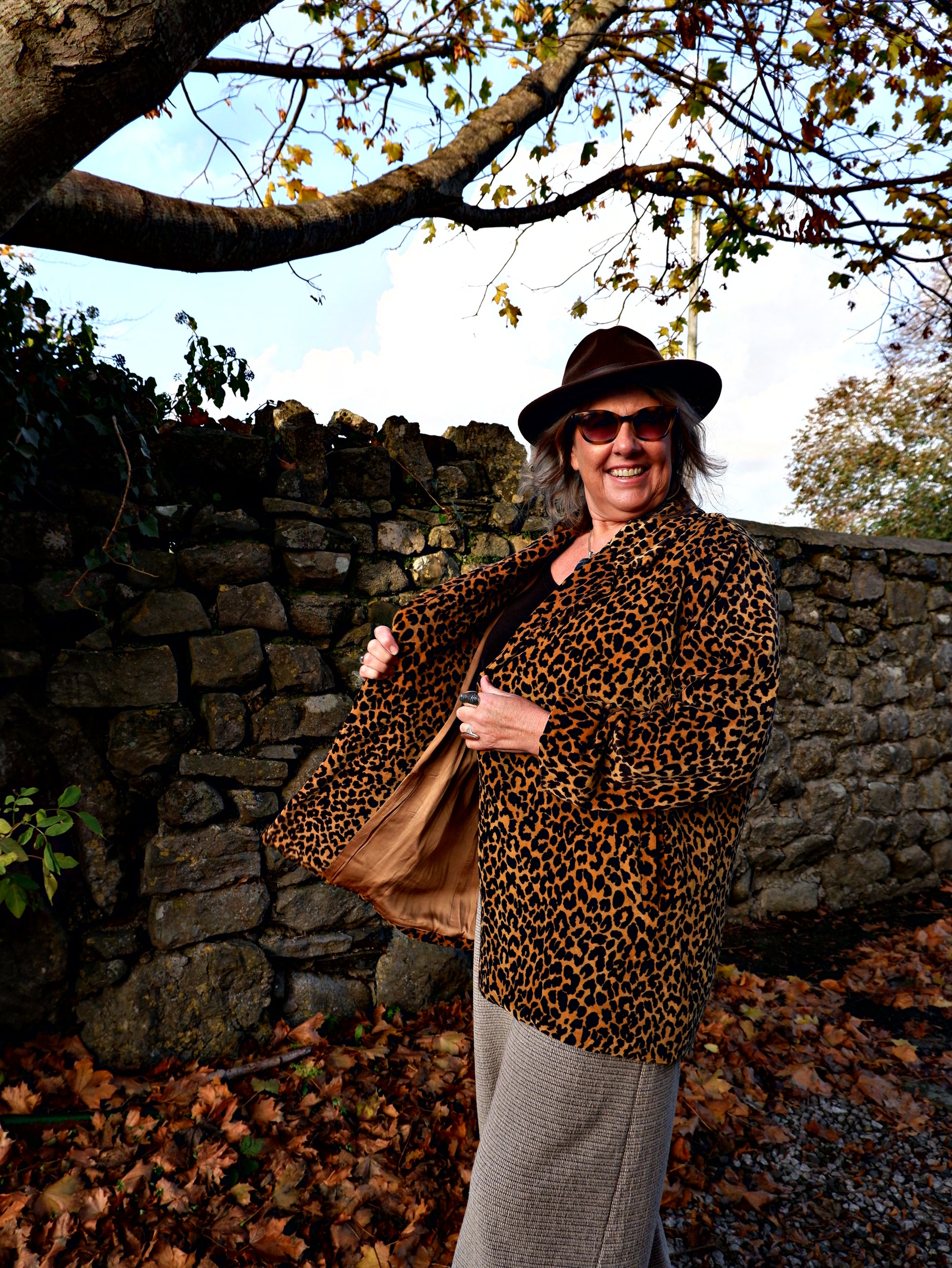 Person wearing a leopard print coat and hat standing against a stone wall