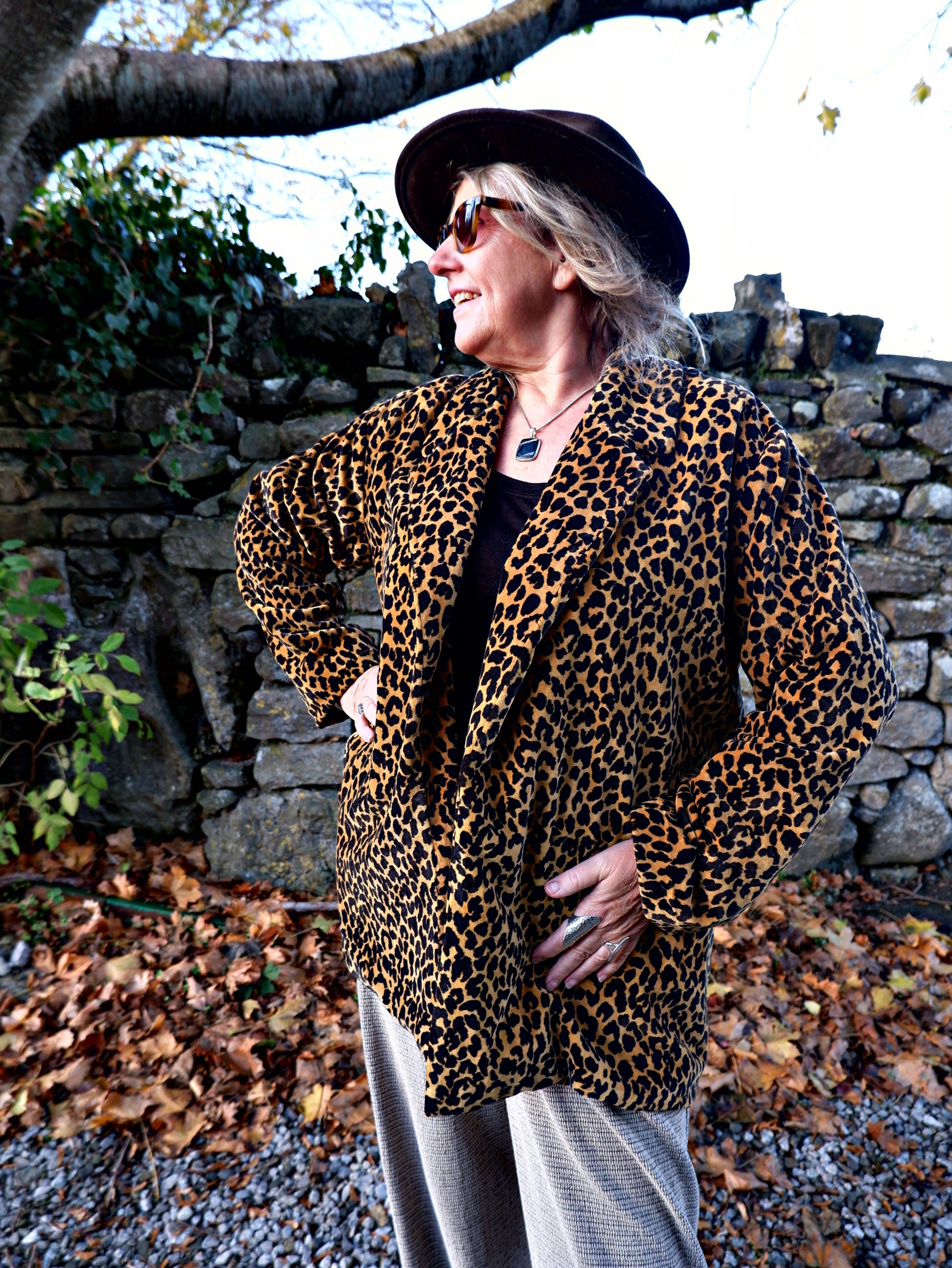 Person wearing a leopard print coat and black hat outdoors.