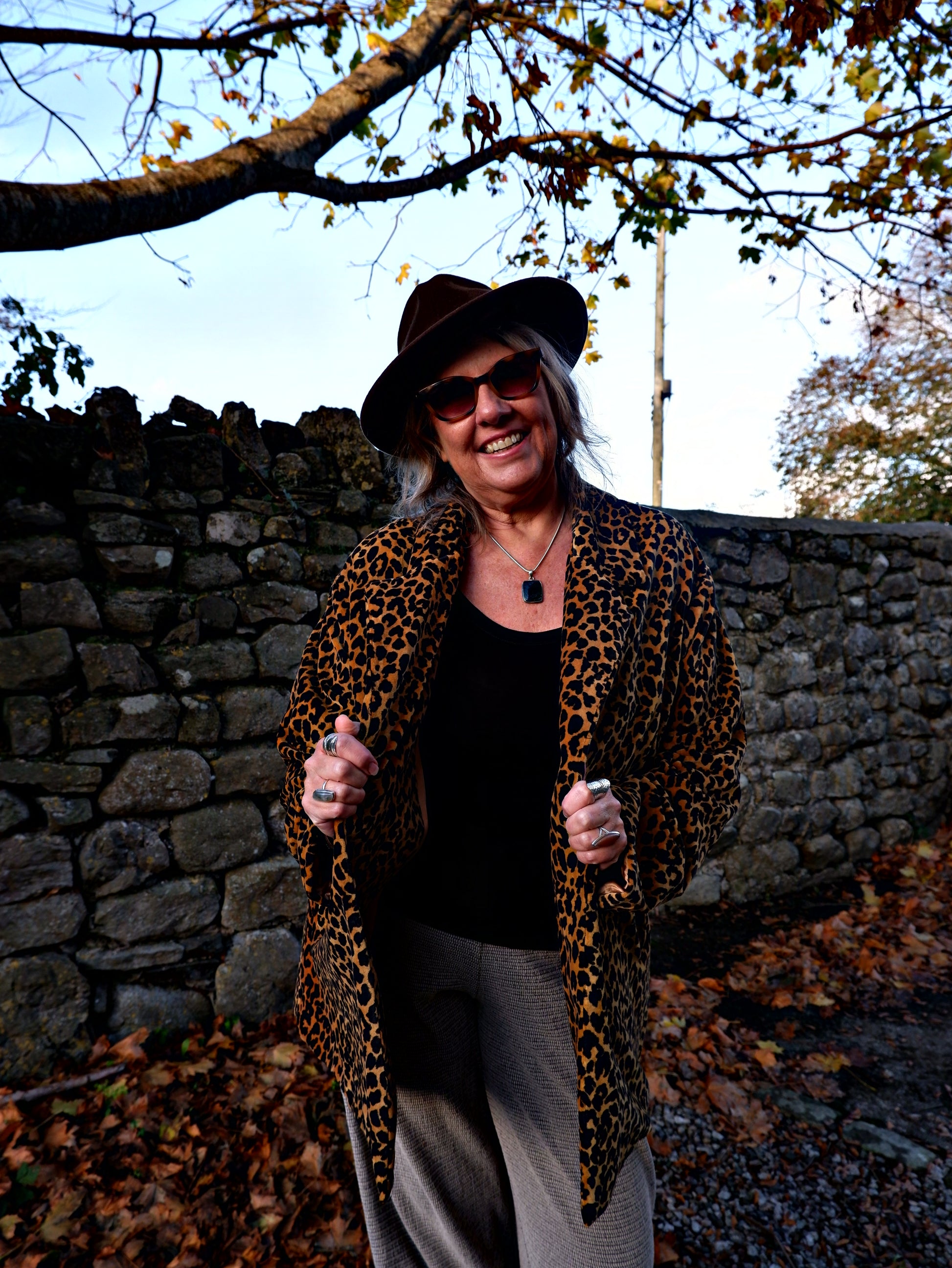 Person wearing a leopard print coat and hat standing against a stone wall